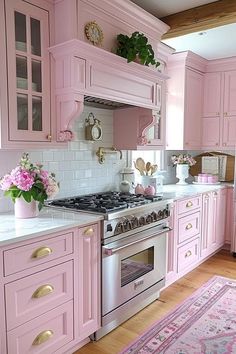 a pink kitchen with white counter tops and gold trim on the cabinets, along with an area rug