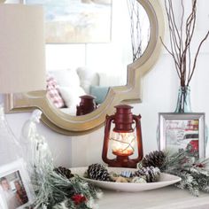 a christmas mantle with pine cones, branches and a lantern on it in front of a mirror