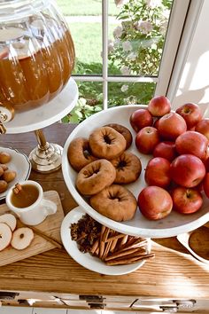 apples, donuts and other snacks are on a table near a glass vase with honey in it