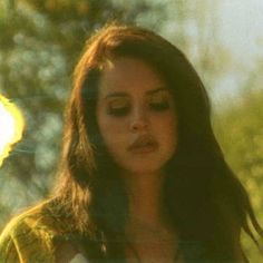 a woman with long brown hair standing in front of trees and looking at her cell phone