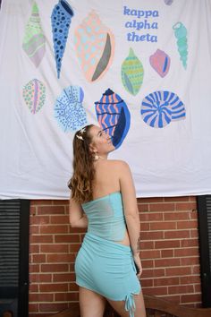 a woman in a short blue dress standing next to a brick wall with a large banner behind her