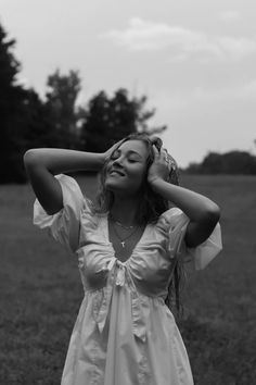 a woman is standing in the grass with her hands on her head and eyes closed