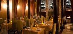 a dining room with tables and chairs covered in yellow cloths, lit by candles