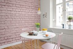 a white table and two pink chairs in front of a brick wall