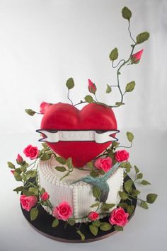 a red heart sitting on top of a cake covered in white frosting and pink roses