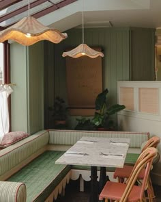 a table and chairs in a small room with green walls, wood flooring and windows