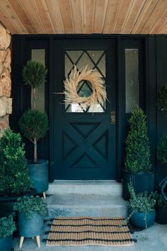 a black front door with potted plants and a wreath on the side entrance to a house