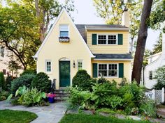 a yellow house with green shutters and trees in the front yard is surrounded by greenery