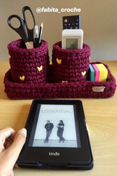 a person is holding a tablet near some crocheted items