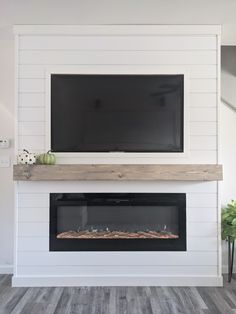 a flat screen tv mounted on the wall above a fireplace in a living room with wood flooring