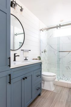 a white toilet sitting next to a walk in shower under a bathroom mirror above a sink