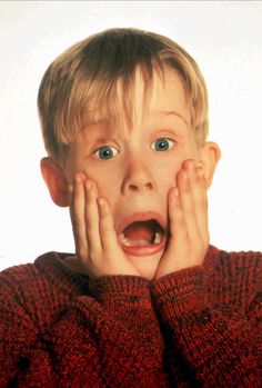 a young boy with his hands on his face, making a silly face while looking at the camera