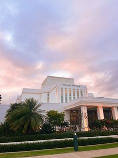 a large white building sitting on top of a lush green field next to a tall palm tree