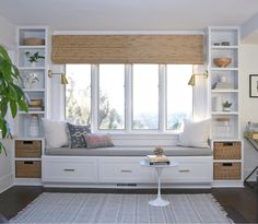 a window seat in the corner of a room with white shelves and drawers on either side