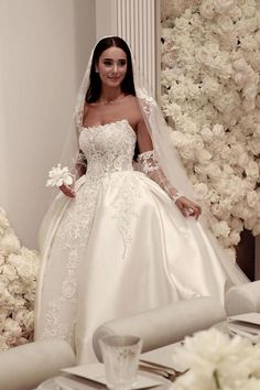 a woman in a wedding dress standing next to a table with white flowers on it