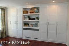 an empty living room with white cupboards and wood floors in front of a window