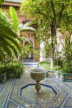 a fountain surrounded by potted plants and greenery in the middle of a courtyard