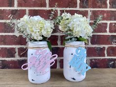 two mason jars with flowers in them sitting on a table next to a brick wall