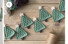 crocheted christmas tree ornaments are displayed on a wooden table next to yarn and twine