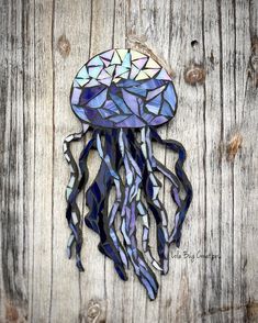 a stained glass jellyfish is hanging on a wooden planked wall with blue, purple and white colors