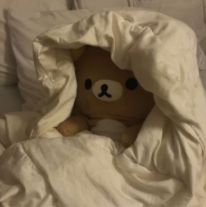 a brown teddy bear sitting in a bed under a white comforter with pillows on it