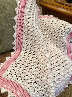 a pink and white crocheted blanket sitting on top of a couch next to a pillow