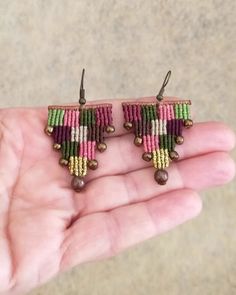 a pair of pink, green and yellow beaded earrings on someone's hand