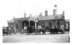 an old black and white photo of people standing in front of a train station with horse drawn carriages