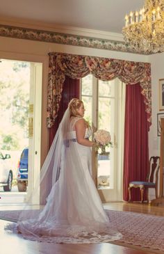 a woman in a wedding dress is standing near a chandelier and holding a bouquet