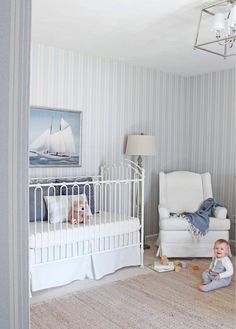 a baby sitting on the floor next to a white crib in a room with striped walls