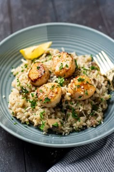 a blue plate topped with rice covered in scallops and lemon wedges next to a fork