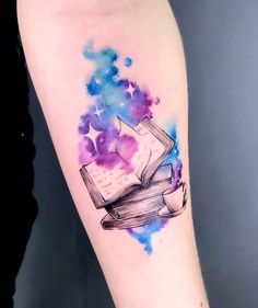 a watercolor tattoo with an open book and stars on it's left arm