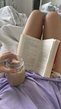 a person laying in bed reading a book and holding a jar of peanut butter next to them