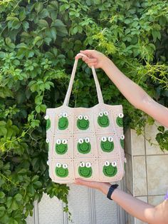 a hand holding a crocheted bag with green eyes on it and two hands