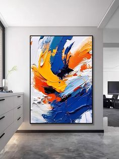 an abstract painting hangs on the wall in a modern kitchen with white cabinets and drawers