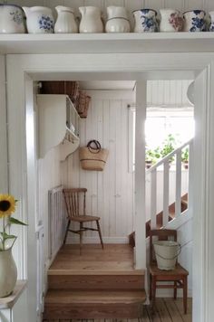 a room with white walls and wooden floors has sunflowers in vases on the shelf