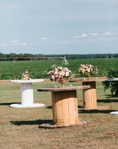 two wooden tables with vases and flowers on them in the middle of a field