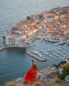 a woman in a red dress looking out over the water at a city and marina