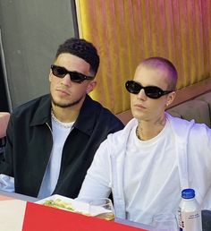 a man and woman sitting at a table with food in front of them, wearing sunglasses