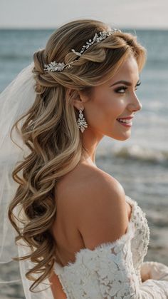 a woman wearing a wedding dress and veil with flowers in her hair, standing on the beach