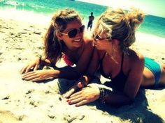 two beautiful women laying on top of a sandy beach