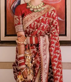 a woman in a red and gold sari is standing next to a large painting