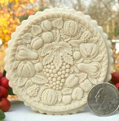 a coin is sitting next to a ceramic plate with grapes on it and leaves in the center