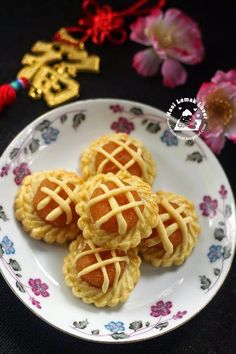 four small pastries on a plate next to some pink flowers and chinese characters in the background