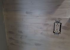 a white toilet sitting in a bathroom next to a wooden paneled wall with a light switch on it