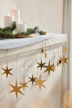 some candles are sitting on top of a mantle with stars hanging from it's sides