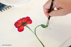 a person is painting a flower with watercolors on white paper and using a pencil