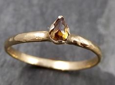 a yellow gold ring with a pear shaped brown diamond in the center, sitting on a gray surface