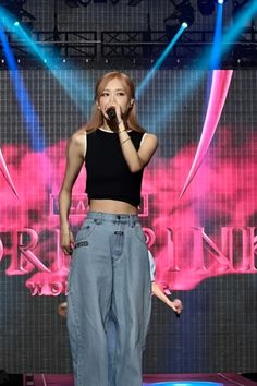 a woman standing on top of a stage holding a microphone in her hand and wearing high waist jeans