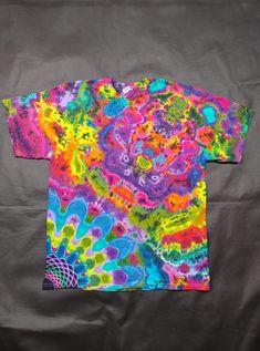 a t - shirt that has been dyed with different colors and patterns on it, sitting on top of a gray surface